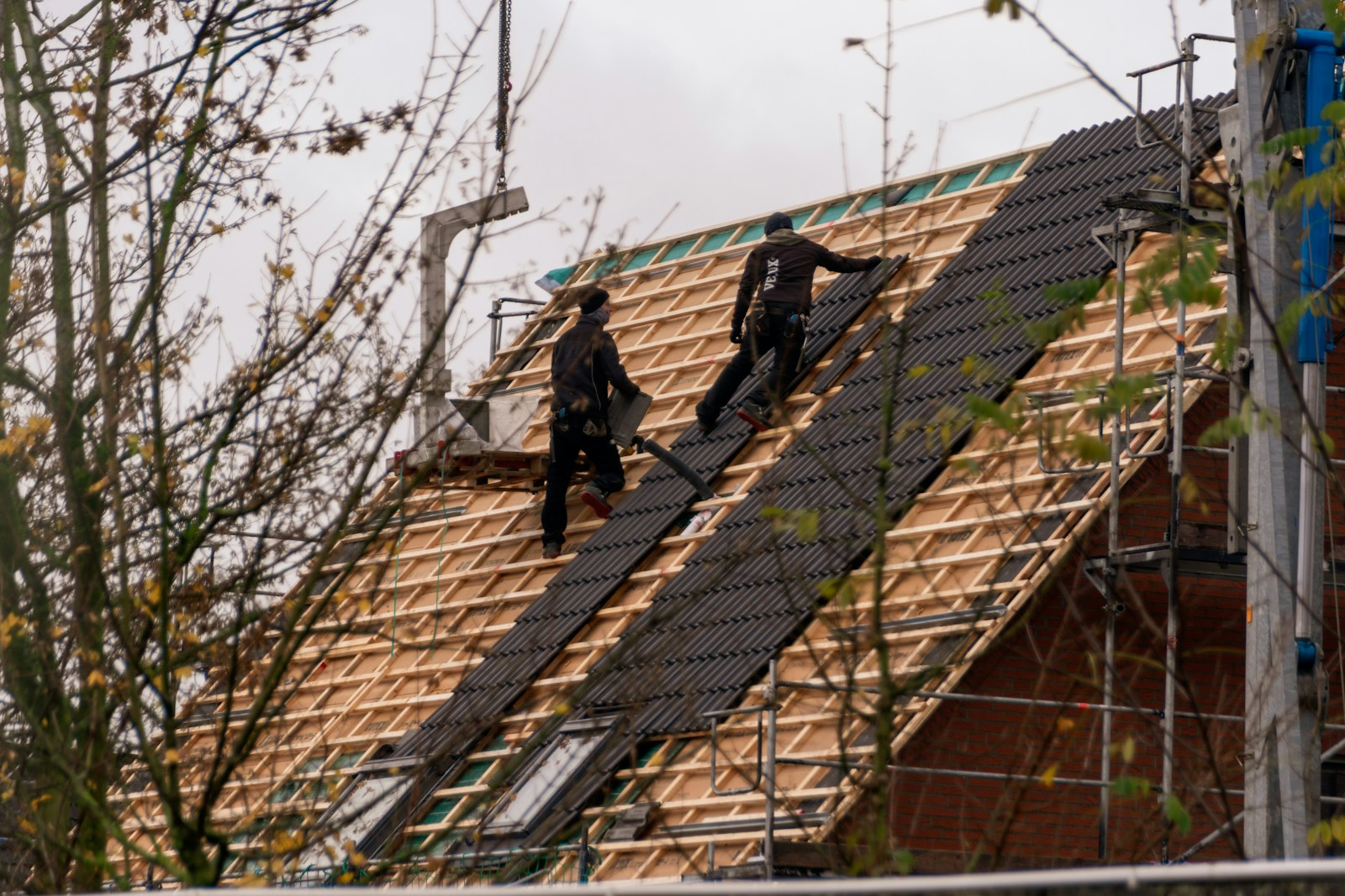 Workers installing shingles on a steep roof